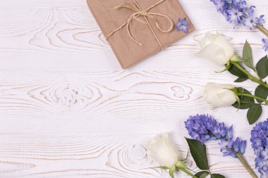 El işi kağıdına sarılı bir hediye kutusu ve mavi sümbül çiçekleri, beyaz bir masanın üstünde beyaz güller. Düz yatıyordu. Metin için alanı kopyala