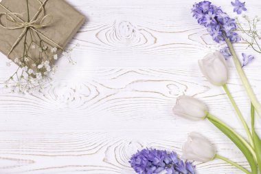 El işi kağıdına sarılı bir hediye kutusu ve mavi sümbül çiçekleri, beyaz bir masanın üstünde beyaz güller. Düz yatıyordu. Metin için alanı kopyala