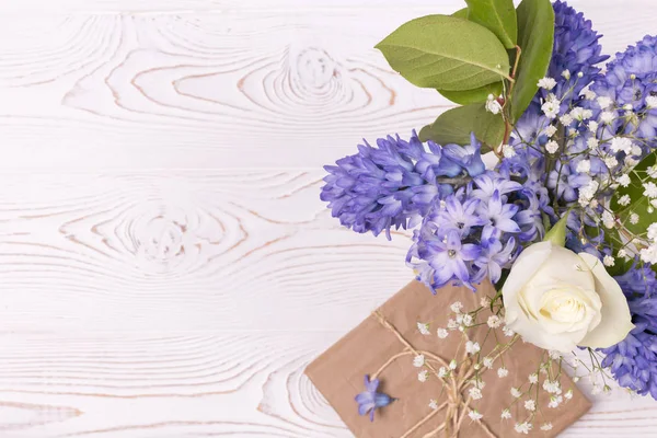 Una confezione regalo avvolta in carta artigianale e fiori di giacinto blu, rose bianche su un piano d'appoggio bianco. Piatto. Copia spazio per testo — Foto Stock