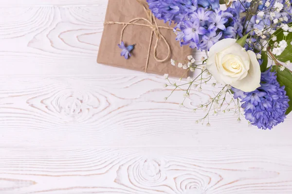 Una confezione regalo avvolta in carta artigianale e fiori di giacinto blu, rose bianche su un piano d'appoggio bianco. Piatto. Copia spazio per testo — Foto Stock