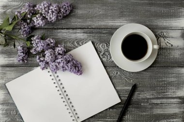 Gri bir ahşap masa üzerinde üstten görünüm bir günlük ya da defter, kalem ve kahve ve mor bir çiçek. Düz tasarım.