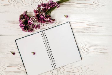 Beyaz ahşap masa üzerinde Üstten Görünüm boş günlüğü veya defter ve mor çiçek. Düz tasarım