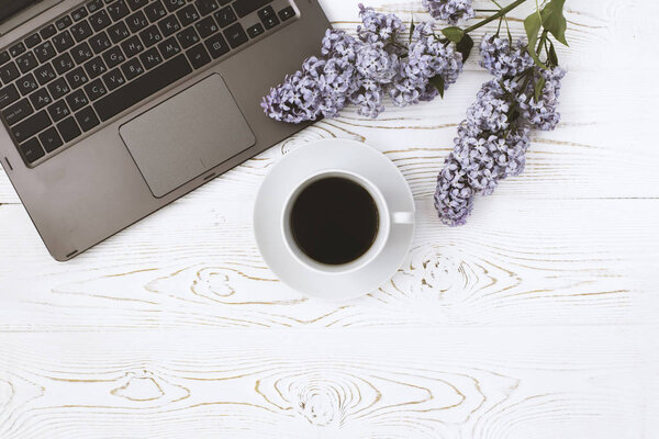 Вид сверху на компьютер и чашку кофе с цветами лилака на белом деревянном столе. Место для текста
