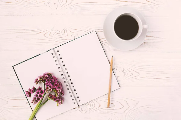 Draufsicht auf ein Tagebuch oder Notizbuch, Bleistift und Tasse Kaffee und eine lila Blume auf einem weißen Holztisch. flache Bauweise — Stockfoto