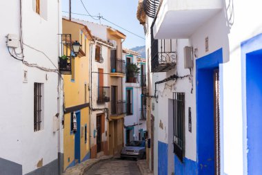 Finestrat, Alicante, Spain - 23 February 2019: Narrow street in the old town with colored houses with shabby plaster and cobblestone stairs. clipart