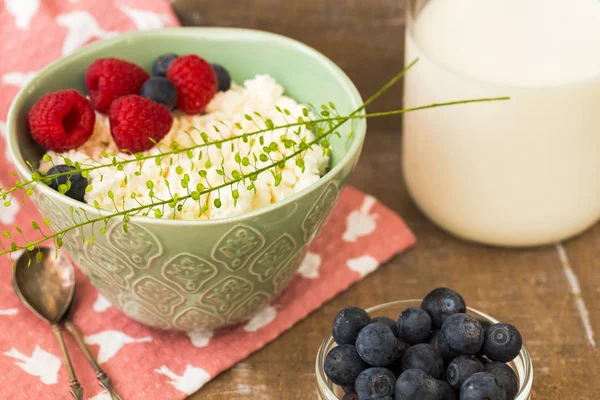 Quark mit frischen Himbeeren und Blaubeeren in einer Schüssel für ein gesundes Frühstück mit reifen Beeren und Milch in einer Glasflasche. — Stockfoto