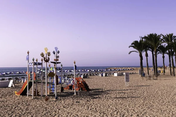 Villajoyosa, Costa Blanca, Spagna - 3 luglio 2018: Spiaggia con palme e complesso per bambini con scivolo sulla sabbia — Foto Stock