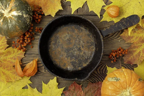 Autumn table for Thanksgiving dinner. Top view of maple leaf on a empty pan and fallen colored leaves on a wooden table. The concept of autumn food.