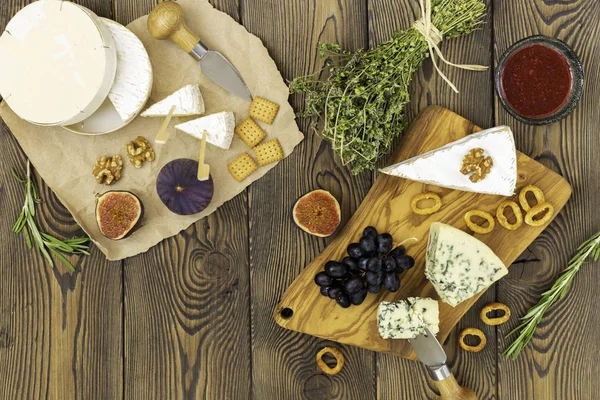 Peynir tabağı reçel, incir, kraker ve otlar ahşap bir arka plan üzerinde servis edilir. Metnin altına yerleştirin. Düz yatıyordu.