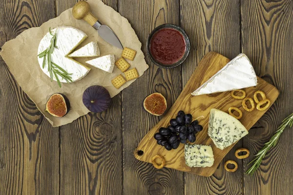 Peynir tabağı reçel, incir, kraker ve otlar ahşap bir arka plan üzerinde servis edilir. Metnin altına yerleştirin. Düz yatıyordu.