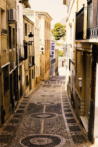 The cozy street of the old European city of Relleu is paved with cobblestones in the form of a picture. Mediterranean architecture in Spain