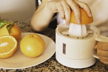 Portakal yarım ve taze sıkılmış narenciye ile bir narenciye sıkacağı tutan bir gençlerin elleri Detay