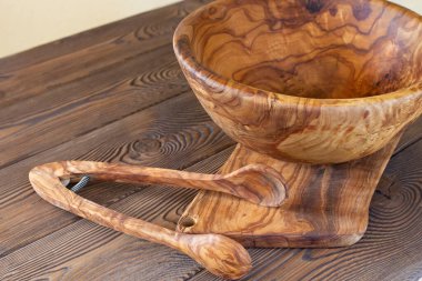 Ahşap mutfak aletleri kesim tahtası ve kase, ahşap masa arkasında salata maşası.