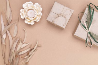 Sonbahar kompozisyonu. Kraft kağıdına sarılı hediyeler, sonbahar okaliptüs yaprakları, bej arkaplanda çiçek şeklinde mum. Düz konum, üst görünüm, kopyalama alanı.