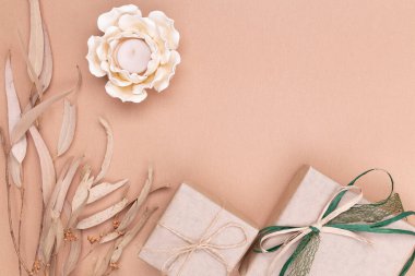 Sonbahar kompozisyonu. Kraft kağıdına sarılı hediyeler, sonbahar okaliptüs yaprakları, bej arkaplanda çiçek şeklinde mum. Düz konum, üst görünüm, kopyalama alanı.