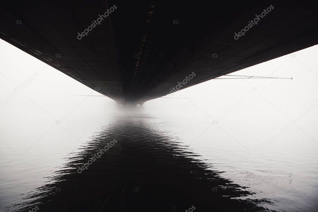 Fog under the bridge . Haze over Danube water . Bridge underside with reflection in the water  