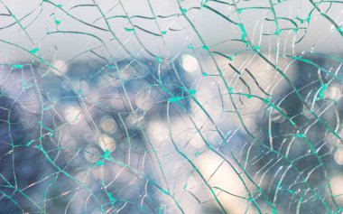 Kırık cam levha, yüzey keskin çatlaklarla kaplı. Bulanık arka plan şehir ışıklarını ve sisli gökyüzünü ortaya çıkarıyor. Kırık cam parçalarının oluşturduğu soyut doku