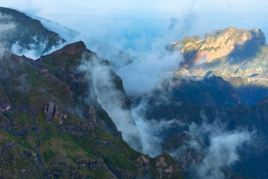 Pico Ruivo, Madeira 'nın engebeli tepelerinde sis örer ve dramatik dağ manzarası üzerinde mistik bir atmosfer yaratır. Gölgeler ve güneş ışığı adanın vahşi ve doğal güzelliğini vurgular.