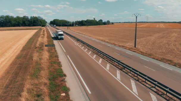 Аерофотозйомка автомобілів і вантажівок, що йдуть на промисловий сільськогосподарський завод і склад в сільській місцевості. Логістика та транспортна концепція. Поля жита, пшениця, що оточує рослину — стокове відео