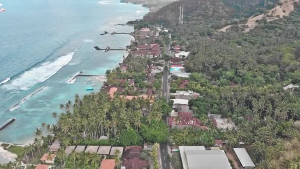 Воздушные съемки: Летающие над тропическим островом Бали береговая линия, местная деревня и курорты к океану с волнами, пальмами, серым песком и скалами. 4K — стоковое видео