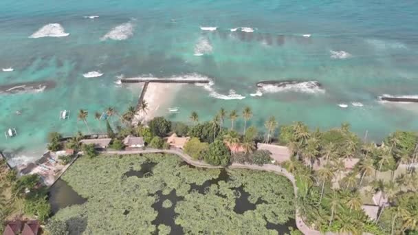 Imágenes aéreas: Volando por encima de la isla tropical de la costa de Bali, pueblo local y resorts hacia un océano con olas, palmeras, arena gris y acantilados. 4K — Vídeos de Stock