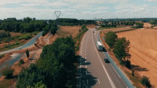 Vista aérea del tráfico de automóviles y camiones que van a la planta de fabricación agrícola industrial y almacén en el campo. Campos de centeno, trigo que rodea la planta 4K — Vídeo de stock