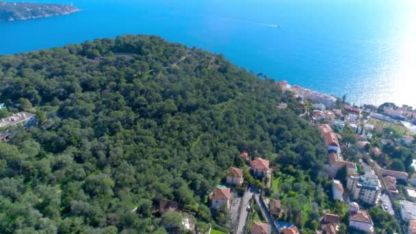 Pueblo mediterráneo cerca de Niza en las verdes colinas bajo la luz del sol. tejados y calles estrechas abajo. montañas y el mar en la distancia. Verano en Francia desde la vista aérea 4K drone — Vídeo de stock