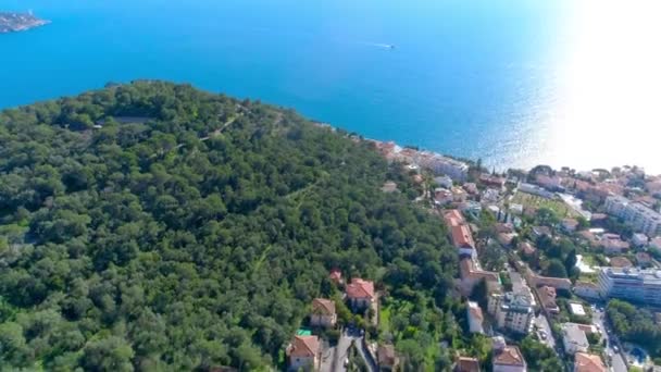 Pueblo mediterráneo cerca de Niza en las verdes colinas bajo la luz del sol. tejados y calles estrechas abajo. montañas y el mar en la distancia. Verano en Francia desde la vista aérea 4K drone — Vídeo de stock