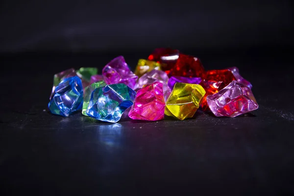 Multicolored crystals, transparent stones similar to lollipops, ice cubes on a black wood background.