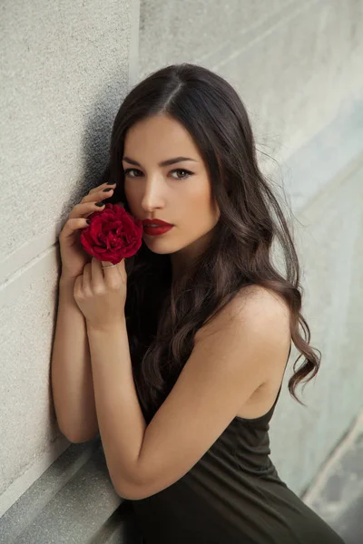 彼女の顔に近いバラを保持している美しい若い女性にもたれかかられて白い壁 屋外のポートレート ロイヤリティフリーのストック写真