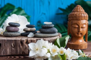 Gri Zen taşlarından piramitler, güzel taze beyaz çiçekler yeşil yapraklar ve ahşap arka planda Buda heykeli. Uyum kavramı, denge ve meditasyon, spa, masaj, rahatlama