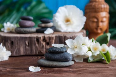 Gri Zen taşlarından piramitler, güzel taze beyaz çiçekler yeşil yapraklar ve ahşap arka planda Buda heykeli. Uyum kavramı, denge ve meditasyon, spa, masaj, rahatlama