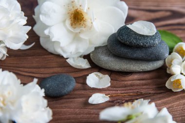 Gri Zen taşlarından piramitler, güzel taze beyaz çiçekler, ahşap arka planda yeşil yapraklar. Uyum kavramı, denge ve meditasyon, spa, masaj, rahatlama