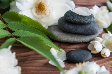 Gri Zen taşlarından piramitler, güzel taze beyaz çiçekler, ahşap arka planda yeşil yapraklar. Uyum kavramı, denge ve meditasyon, spa, masaj, rahatlama