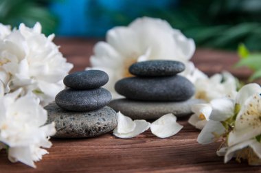 Gri Zen taşlarından piramitler, güzel taze beyaz çiçekler, ahşap arka planda yeşil yapraklar. Uyum kavramı, denge ve meditasyon, spa, masaj, rahatlama