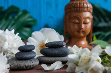 Gri Zen taşlarından piramitler, güzel taze beyaz çiçekler yeşil yapraklar ve ahşap arka planda Buda heykeli. Uyum kavramı, denge ve meditasyon, spa, masaj, rahatlama