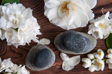 Gri Zen taşlarından piramitler, güzel taze beyaz çiçekler, ahşap arka planda yeşil yapraklar. Uyum kavramı, denge ve meditasyon, spa, masaj, rahatlama