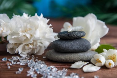 Gri Zen taşlarından piramitler, güzel taze beyaz çiçekler, ahşap arka planda yeşil yapraklar. Uyum kavramı, denge ve meditasyon, spa, masaj, rahatlama