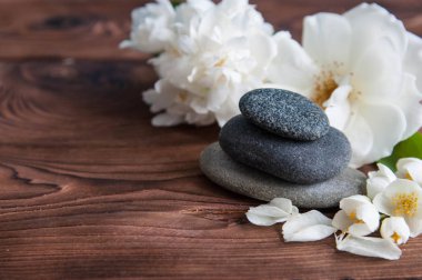 Gri Zen taşlarından piramitler, güzel taze beyaz çiçekler, ahşap arka planda yeşil yapraklar. Uyum kavramı, denge ve meditasyon, spa, masaj, rahatlama