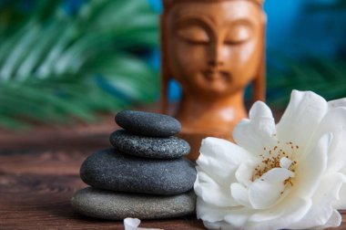 Gri Zen taşlarından piramitler, güzel taze beyaz çiçekler yeşil yapraklar ve ahşap arka planda Buda heykeli. Uyum kavramı, denge ve meditasyon, spa, masaj, rahatlama