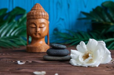 Gri Zen taşlarından piramitler, güzel taze beyaz çiçekler yeşil yapraklar ve ahşap arka planda Buda heykeli. Uyum kavramı, denge ve meditasyon, spa, masaj, rahatlama