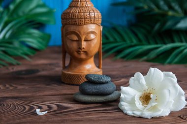 Gri Zen taşlarından piramitler, güzel taze beyaz çiçekler yeşil yapraklar ve ahşap arka planda Buda heykeli. Uyum kavramı, denge ve meditasyon, spa, masaj, rahatlama