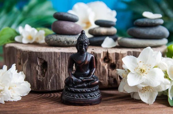 Gri Zen taşlarından piramitler, güzel taze beyaz çiçekler yeşil yapraklar ve ahşap arka planda Buda heykeli. Uyum kavramı, denge ve meditasyon, spa, masaj, rahatlama