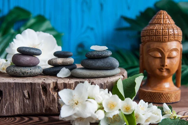 Gri Zen taşlarından piramitler, güzel taze beyaz çiçekler yeşil yapraklar ve ahşap arka planda Buda heykeli. Uyum kavramı, denge ve meditasyon, spa, masaj, rahatlama