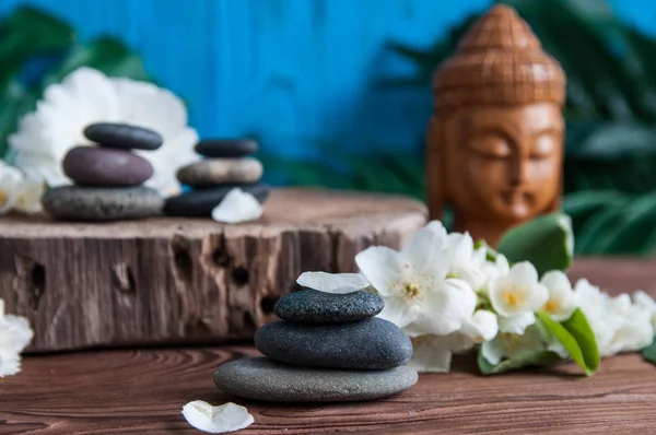 Gri Zen taşlarından piramitler, güzel taze beyaz çiçekler yeşil yapraklar ve ahşap arka planda Buda heykeli. Uyum kavramı, denge ve meditasyon, spa, masaj, rahatlama