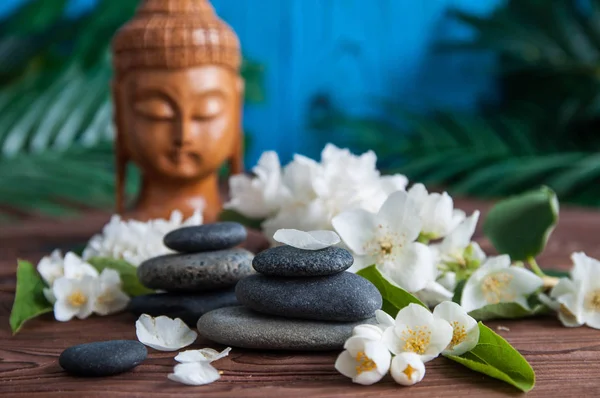 Gri Zen taşlarından piramitler, güzel taze beyaz çiçekler yeşil yapraklar ve ahşap arka planda Buda heykeli. Uyum kavramı, denge ve meditasyon, spa, masaj, rahatlama