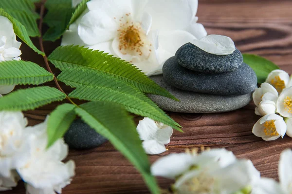 Pyramids of gray zen stones with beautiful fresh white flowers green leaves on wooden background. Concept of harmony, balance and meditation, spa, massage, relax