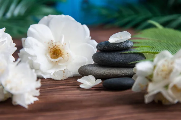 Pyramids of gray zen stones with beautiful fresh white flowers green leaves on wooden background. Concept of harmony, balance and meditation, spa, massage, relax