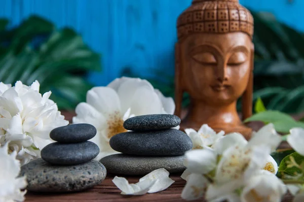 Gri Zen taşlarından piramitler, güzel taze beyaz çiçekler yeşil yapraklar ve ahşap arka planda Buda heykeli. Uyum kavramı, denge ve meditasyon, spa, masaj, rahatlama