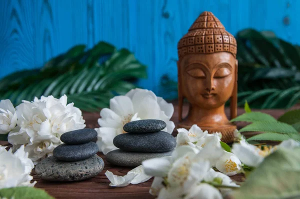 Gri Zen taşlarından piramitler, güzel taze beyaz çiçekler yeşil yapraklar ve ahşap arka planda Buda heykeli. Uyum kavramı, denge ve meditasyon, spa, masaj, rahatlama